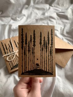 someone is holding up two cards with trees on them and a house in the woods