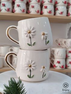 two white coffee mugs with daisies on them are stacked on top of each other