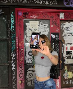 a woman taking a selfie with her cell phone in front of a graffiti covered building