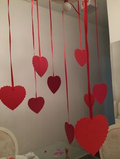 red paper hearts hanging from the ceiling in front of a white wall with chairs and table