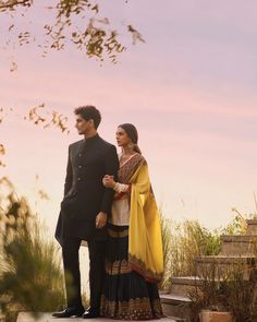 a man and woman standing next to each other on top of a wooden platform in front of tall grass