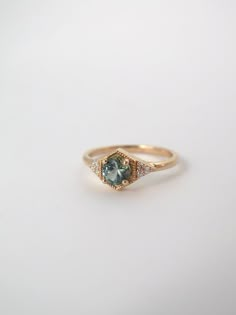 a gold ring with an aqua and white diamond in the center on a white surface