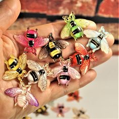 a person holding a bunch of different colored bee charms in their hand with the words bees on them