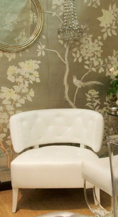 a white chair sitting next to a table with flowers on it and a mirror behind it