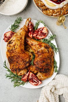 two pieces of chicken on a plate with tomatoes and rosemary