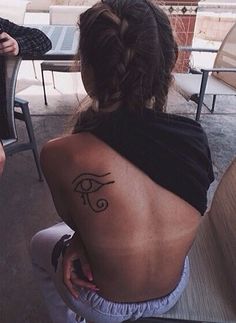 a woman with a tattoo on her back sitting in front of a table and chairs