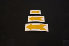 three yellow arrows pointing in opposite directions on a black surface with white paper cut out