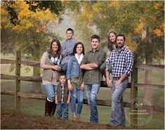 a family posing for a photo in front of a fence with fall leaves on the trees