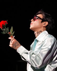 a man with tattoos holding a rose in his right hand and looking up at the sky