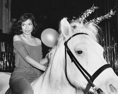 a woman riding on the back of a white horse next to a bunch of balloons