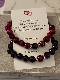 two bracelets with red and black beads are on display in a gift card box