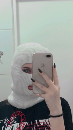 a woman wearing a white mask holding up a cell phone