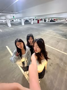 three girls standing in an empty parking lot pointing at the camera with their fingers up