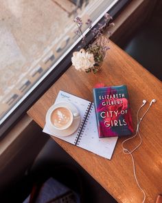 a table with a book and headphones on top of it next to a cup of coffee