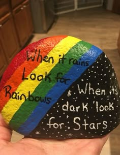 a hand holding a rock with writing on it that says when it rains, look for rainbows