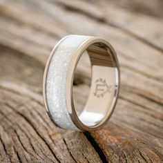 a wedding ring with white sand inlays on it sitting on a piece of wood