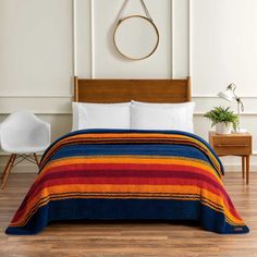 a bed with a colorful blanket on top of it next to a white chair and potted plant