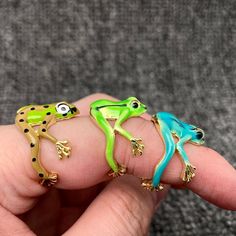 three different colored frog rings sitting on top of each other's fingers in front of a gray background