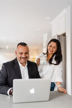 a man and woman standing in front of a laptop computer holding up a cup while smiling at each other