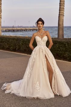 a woman in a wedding dress standing on the street near some palm trees and water