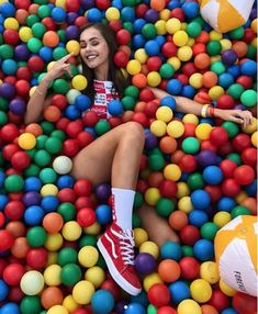 a woman sitting in a ball pit with her feet on the ground and balls all around her