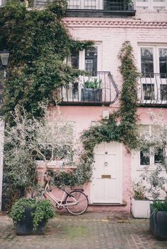 a bicycle parked in front of a pink building with ivy growing on it's side