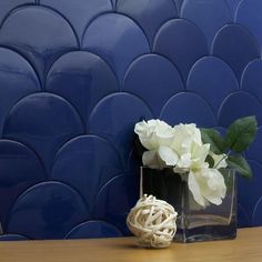 a vase with white flowers sitting on a table next to a blue tile wall behind it