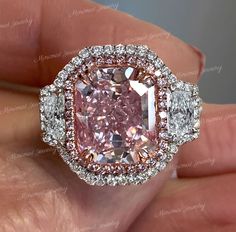 a pink diamond surrounded by two white diamonds in a halo setting with an oval center stone