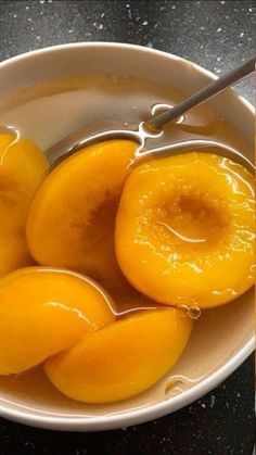 a white bowl filled with sliced peaches on top of a black counter next to a spoon