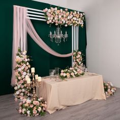 a table with flowers and candles on it in front of a green wall decorated with pink roses