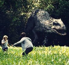 two people are playing in the grass near a dinosaur