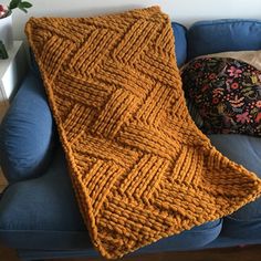 an orange knitted blanket sitting on top of a blue couch next to a pillow