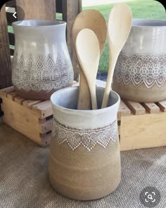 three wooden spoons and two ceramic bowls with lace on them sitting on a table