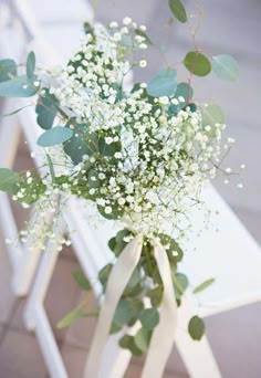 a bouquet of baby's breath sitting on top of a white chair with greenery