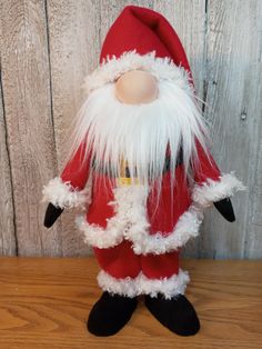 a red and white santa claus doll on a wooden table next to a wood wall