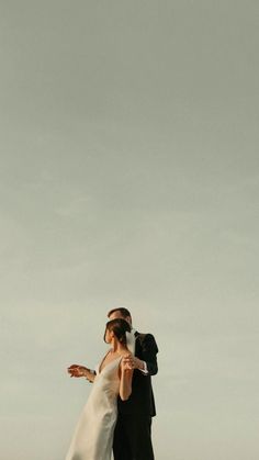 a bride and groom standing on top of a hill with their arms around each other