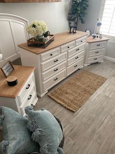 a bedroom with white dressers and wooden flooring next to a large window on the wall