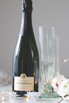 a bottle of champagne next to two glasses with flowers on the side and one glass filled with water