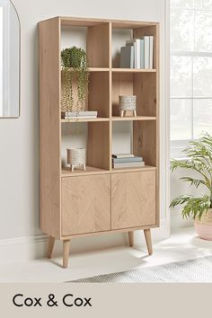 a wooden bookcase with plants and books on it in front of a white wall