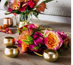 a bouquet of flowers sitting on top of a wooden table next to two gold cups