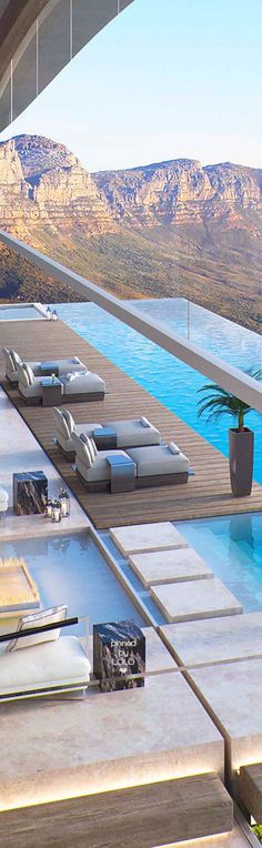 an outdoor swimming pool with chaise lounges and mountains in the backgroud