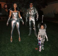 a man and woman dressed in silver standing next to a child wearing an astronaut suit