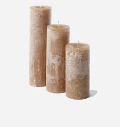 three pillar candles are lined up against a white background, each with a single candle in the middle