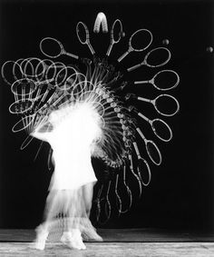 a woman walking past a sculpture made out of tennis racquets on top of a wooden floor