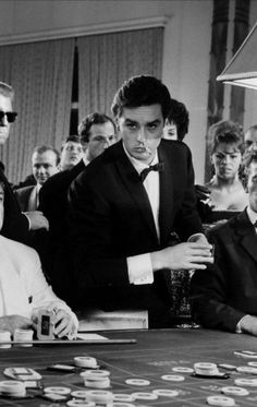 black and white photograph of men playing cards at a casino table in front of other people