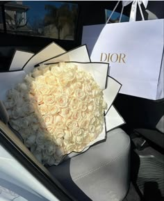 a bouquet of white roses sits in the back seat of a car, next to a dior bag