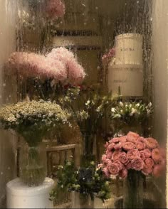 flowers in vases sitting on a window sill behind a rain soaked glass door