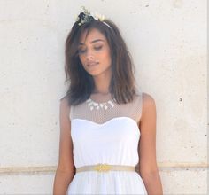 a woman wearing a white dress with a flower crown on her head standing in front of a wall