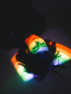 a woman laying down with her head on the ground in front of a rainbow light