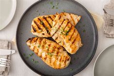 two pieces of grilled chicken on a plate next to silverware and utensils